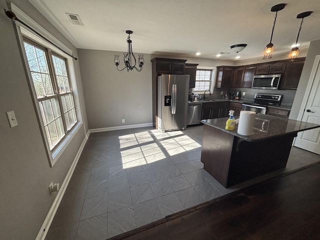 kitchen featuring appliances with stainless steel finishes, a center island, decorative backsplash, sink, and hanging light fixtures