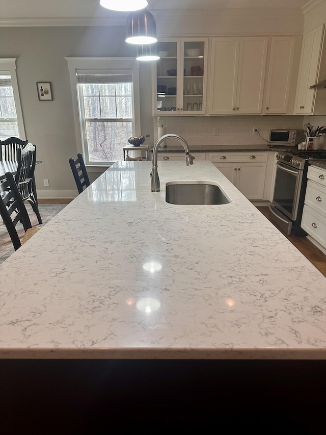 kitchen with pendant lighting, sink, light stone countertops, ornamental molding, and stainless steel range oven