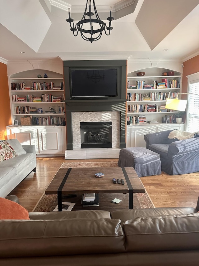 living room featuring a tray ceiling, crown molding, an inviting chandelier, built in features, and a fireplace