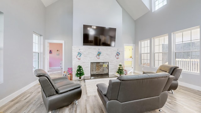 living room featuring light hardwood / wood-style floors, a stone fireplace, and a high ceiling