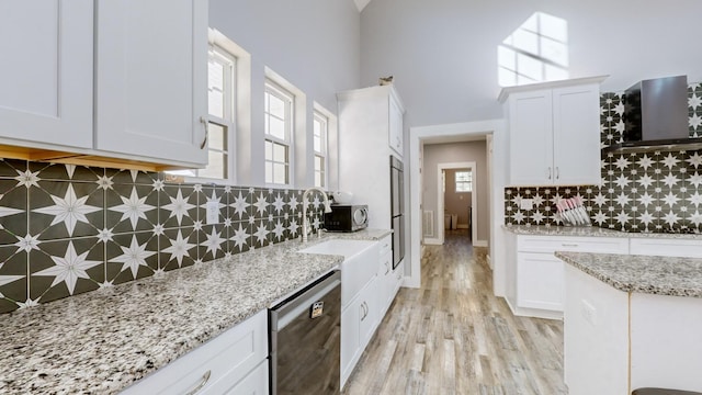 kitchen with appliances with stainless steel finishes, tasteful backsplash, white cabinetry, and wall chimney range hood