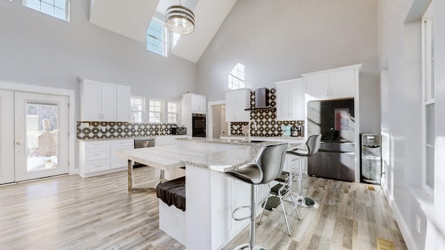 kitchen with white cabinetry, decorative backsplash, black refrigerator, and a high ceiling