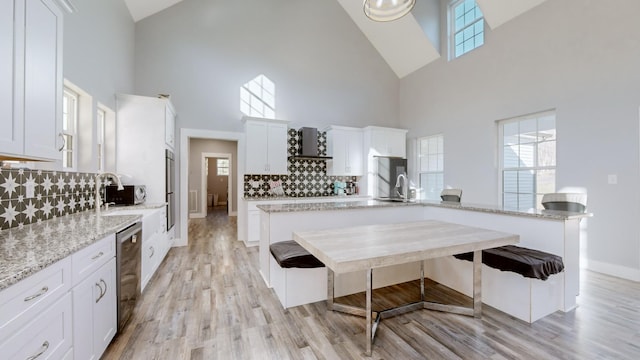 kitchen with light stone countertops, a towering ceiling, appliances with stainless steel finishes, tasteful backsplash, and white cabinetry