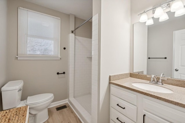 bathroom with hardwood / wood-style flooring, toilet, vanity, and tiled shower