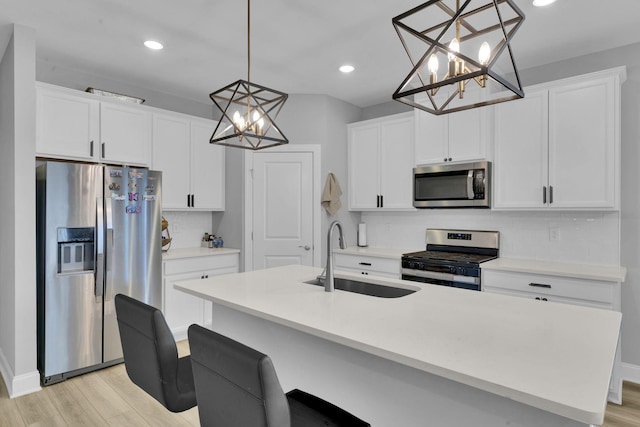 kitchen with white cabinetry, sink, hanging light fixtures, light hardwood / wood-style floors, and appliances with stainless steel finishes