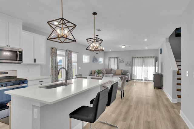 kitchen featuring white cabinetry, sink, hanging light fixtures, a center island with sink, and appliances with stainless steel finishes