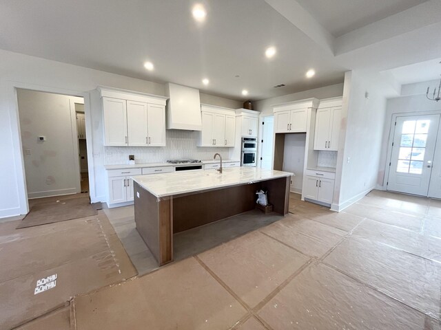 kitchen featuring a kitchen island with sink, light stone counters, white cabinetry, and premium range hood