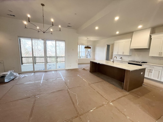 kitchen featuring hanging light fixtures, premium range hood, white cabinets, and an island with sink