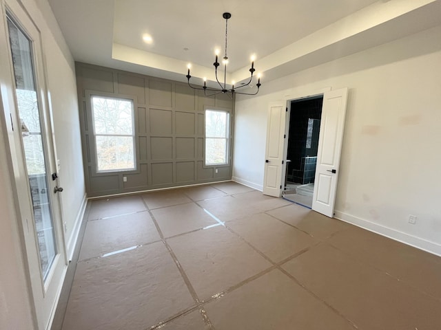 unfurnished dining area with plenty of natural light, a tray ceiling, and a chandelier