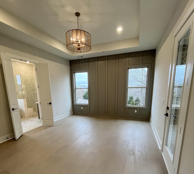 empty room with a raised ceiling, a healthy amount of sunlight, light wood-style flooring, and an inviting chandelier