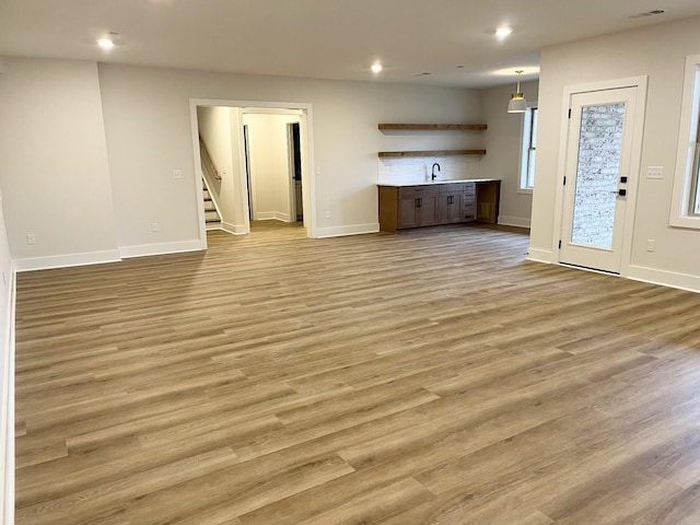 unfurnished living room featuring light wood-type flooring, stairs, a sink, and recessed lighting