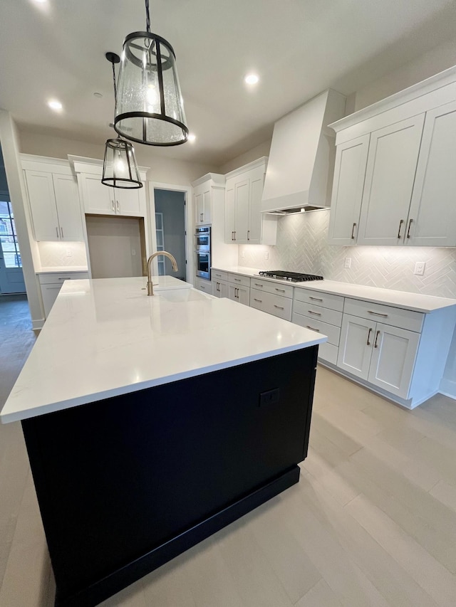 kitchen with stainless steel appliances, premium range hood, a sink, tasteful backsplash, and a large island with sink