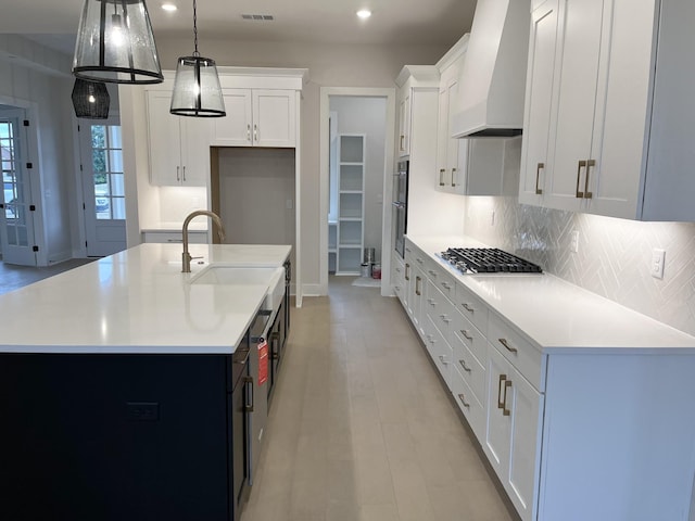 kitchen featuring stainless steel gas cooktop, tasteful backsplash, light countertops, custom range hood, and a sink