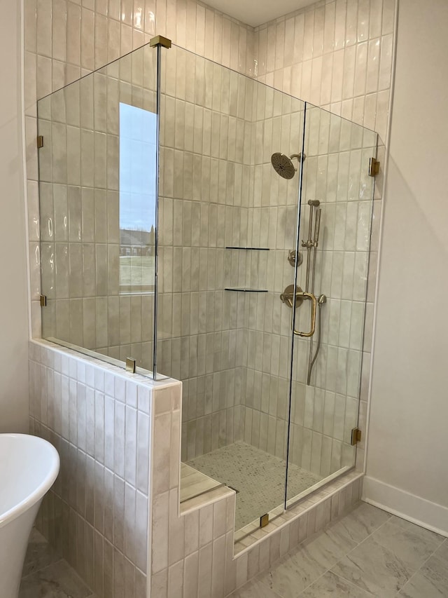 full bathroom with marble finish floor, a stall shower, a soaking tub, and baseboards