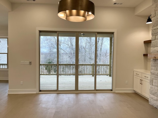 doorway with visible vents, plenty of natural light, baseboards, and wood finished floors