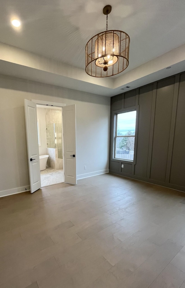 unfurnished bedroom with wood finished floors, an inviting chandelier, connected bathroom, and baseboards