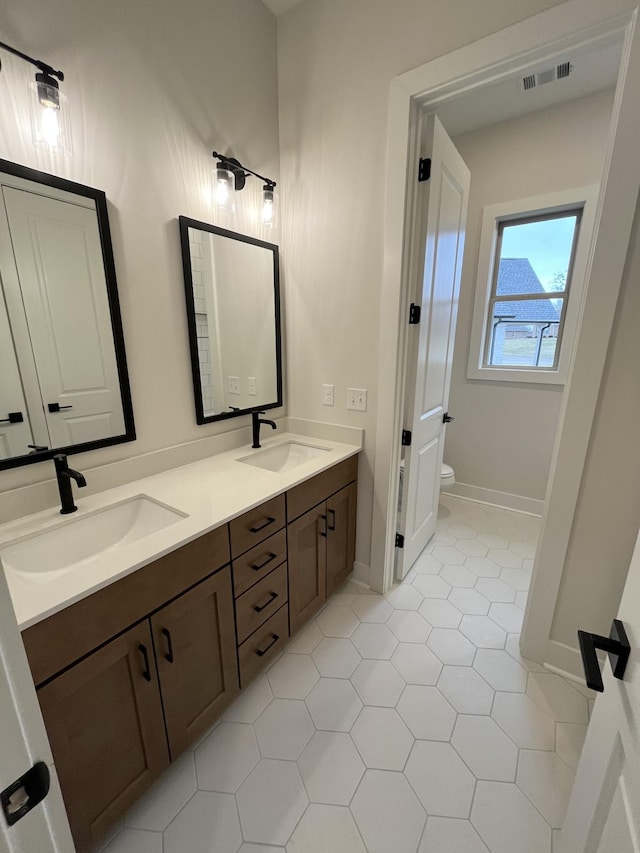 full bathroom featuring toilet, double vanity, visible vents, and a sink