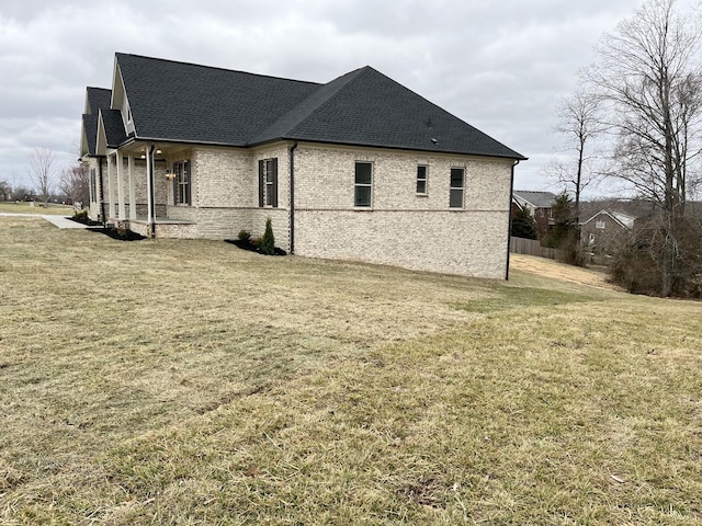 view of property exterior featuring brick siding, a lawn, and a shingled roof