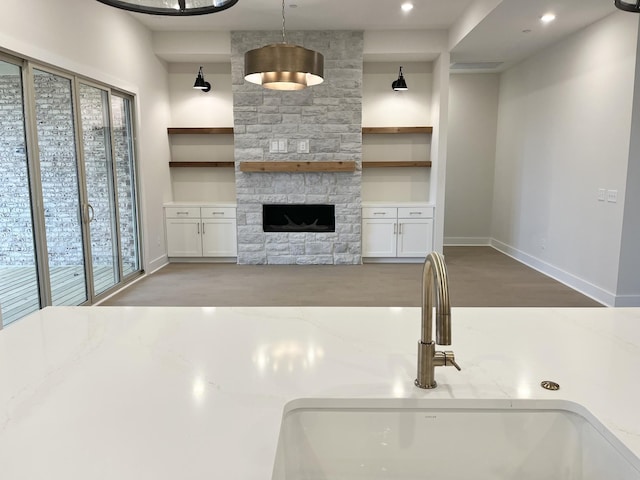 unfurnished living room featuring recessed lighting, a sink, a stone fireplace, wood finished floors, and baseboards