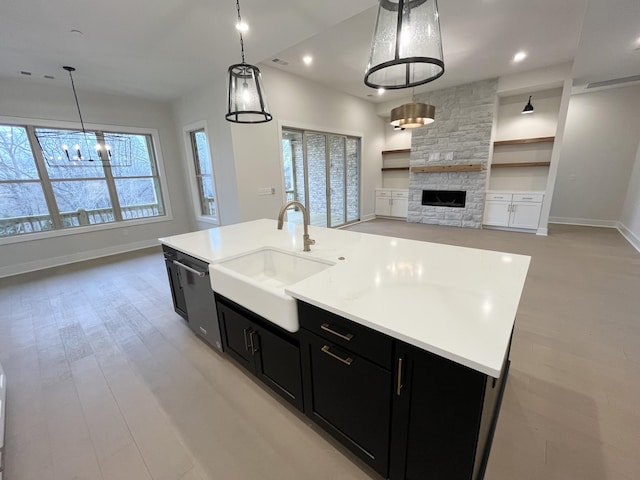 kitchen featuring a sink, light countertops, dark cabinets, and a stone fireplace