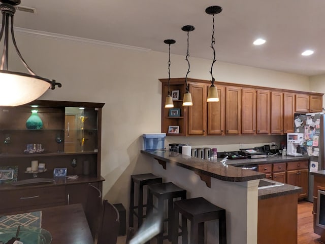 kitchen featuring kitchen peninsula, dark hardwood / wood-style flooring, a breakfast bar, pendant lighting, and dark stone countertops