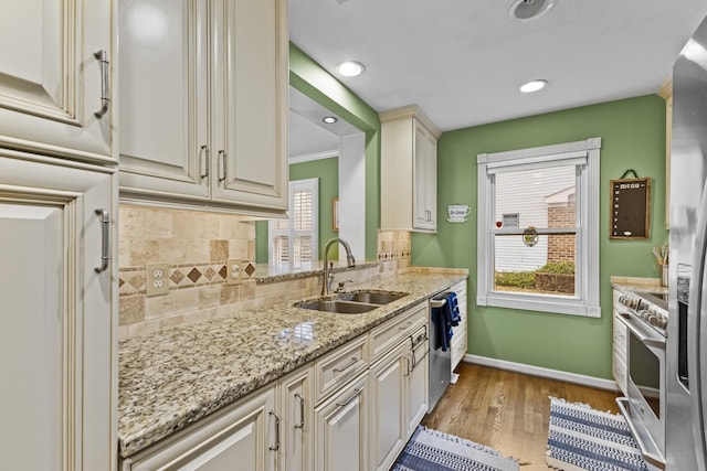 kitchen with appliances with stainless steel finishes, light stone counters, a wealth of natural light, sink, and light hardwood / wood-style floors