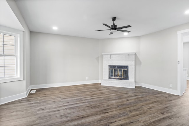 unfurnished living room with ceiling fan, dark hardwood / wood-style flooring, a wealth of natural light, and a brick fireplace