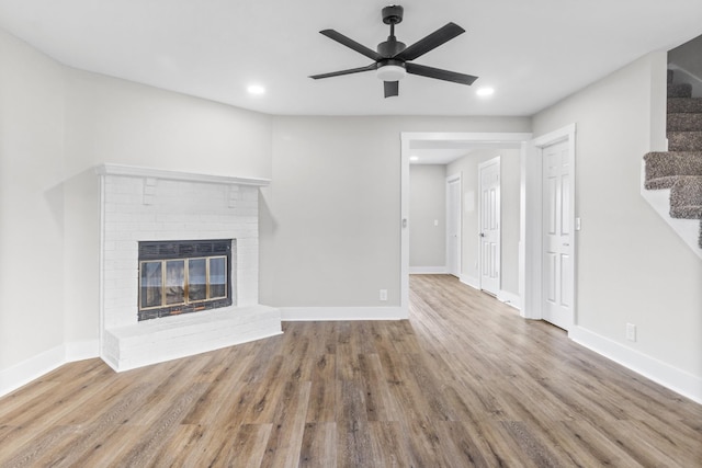 unfurnished living room with ceiling fan, wood-type flooring, and a brick fireplace