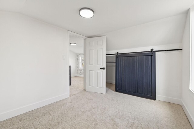 spare room with lofted ceiling, a barn door, and light carpet