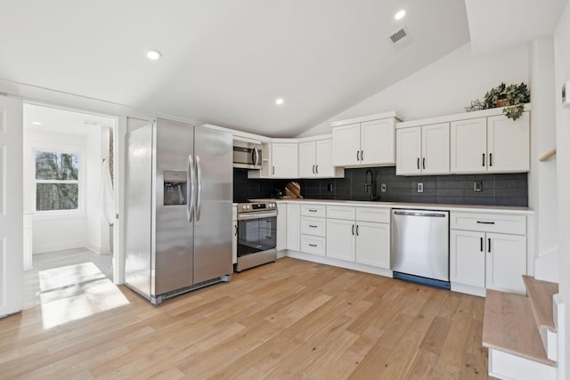 kitchen with stainless steel appliances, lofted ceiling, white cabinets, backsplash, and sink