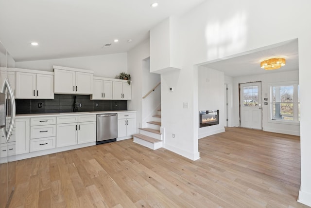 kitchen with stainless steel appliances, sink, white cabinetry, lofted ceiling, and tasteful backsplash