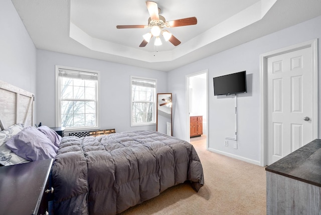 bedroom featuring ensuite bathroom, light colored carpet, ceiling fan, and a tray ceiling