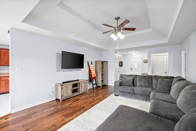 living room featuring a raised ceiling, ceiling fan, and dark hardwood / wood-style flooring