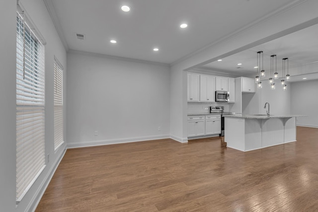 kitchen featuring ornamental molding, stainless steel appliances, decorative light fixtures, white cabinetry, and an island with sink