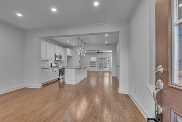 interior space featuring pendant lighting, decorative backsplash, an island with sink, appliances with stainless steel finishes, and white cabinetry