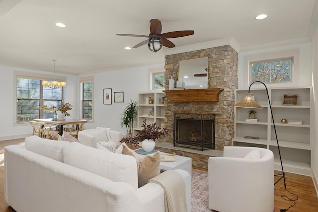 living room with crown molding, a fireplace, wood-type flooring, and ceiling fan with notable chandelier