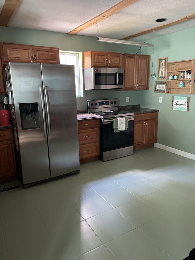 kitchen featuring a textured ceiling, baseboards, appliances with stainless steel finishes, brown cabinetry, and dark countertops