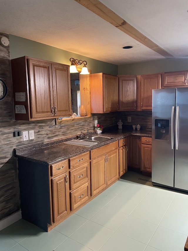 kitchen featuring tasteful backsplash, brown cabinetry, light tile patterned flooring, a sink, and stainless steel fridge