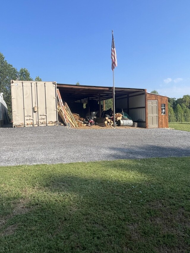 view of outbuilding with a carport, an outdoor structure, and gravel driveway