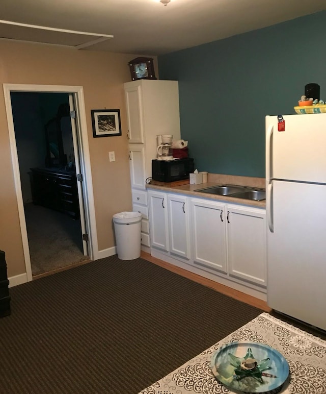 kitchen featuring black microwave, white cabinetry, light countertops, and freestanding refrigerator