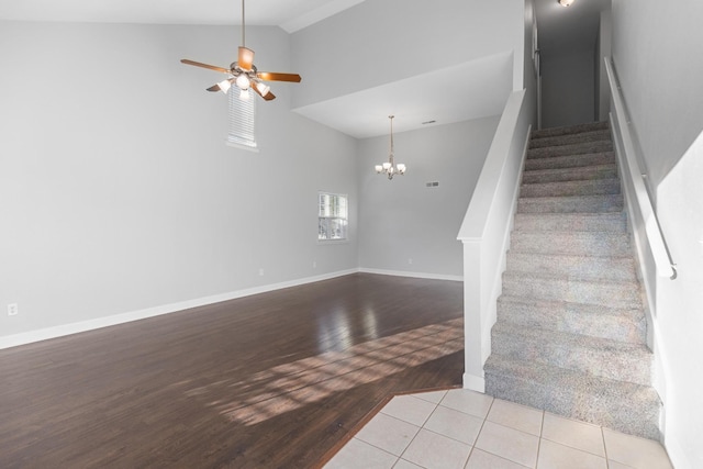 staircase with tile patterned floors, high vaulted ceiling, and ceiling fan with notable chandelier