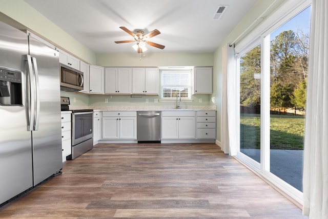 kitchen with appliances with stainless steel finishes, ceiling fan, sink, hardwood / wood-style flooring, and white cabinets