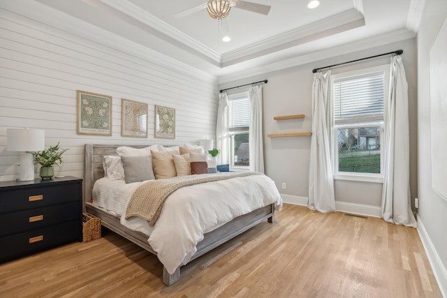 bedroom featuring wood walls, a raised ceiling, crown molding, light hardwood / wood-style flooring, and ceiling fan