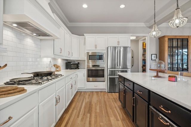 kitchen featuring premium range hood, ornamental molding, stainless steel appliances, white cabinetry, and hanging light fixtures