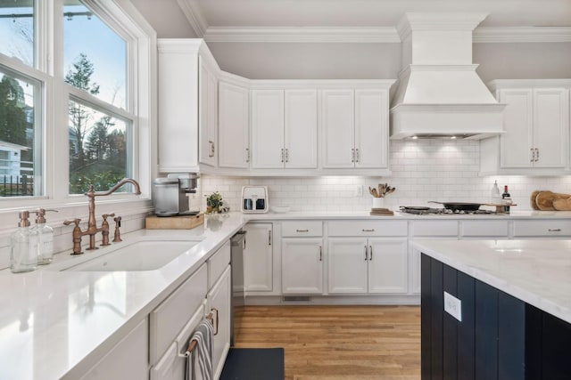 kitchen with white cabinets, backsplash, sink, and premium range hood