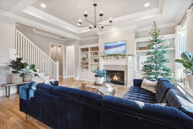 living room with ornamental molding, a tray ceiling, a notable chandelier, light hardwood / wood-style floors, and a tiled fireplace