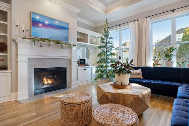 living room featuring built in shelves, light wood-type flooring, ornamental molding, and a tile fireplace