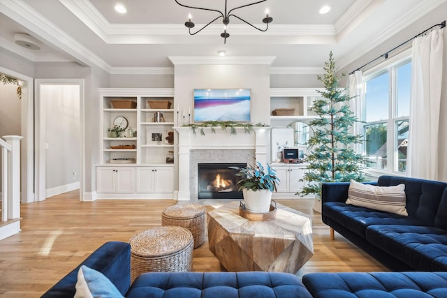 living room with ornamental molding, light wood-type flooring, a fireplace, and a tray ceiling