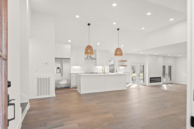 kitchen with pendant lighting, a center island with sink, stainless steel fridge with ice dispenser, tasteful backsplash, and white cabinetry