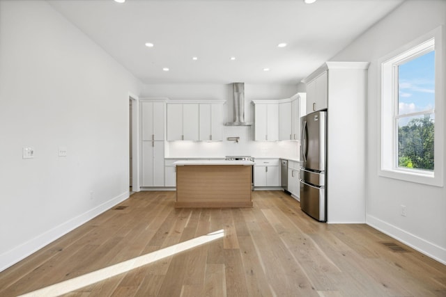 kitchen featuring stainless steel appliances, a healthy amount of sunlight, wall chimney range hood, white cabinets, and a center island